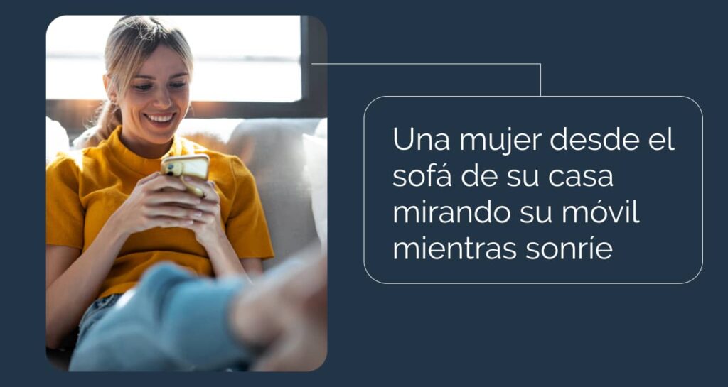 Una mujer desde el sofá de su casa mirando su móvil mientras sonríe mirando la accesibilidad web